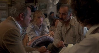 Movie still from “Missing” (1982), directed by Costa-Gavras – A group of people sitting in a room talking to each other; Medium shot, High angle