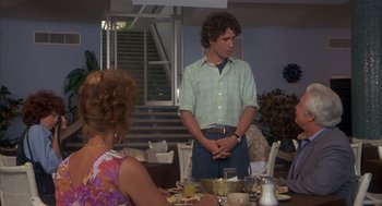 Movie still from “Missing” (1982), directed by Costa-Gavras – A man standing in front of a woman at a dinner table; Medium shot, Over the shoulder angle