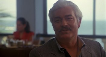 Movie still from “Missing” (1982), directed by Costa-Gavras – An older man with white hair is smiling for the camera; Close Up shot, Over the shoulder angle