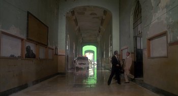 Movie still from “Missing” (1982), directed by Costa-Gavras – Two men walking down a hall way with a car in the background; Extreme Wide shot, High angle