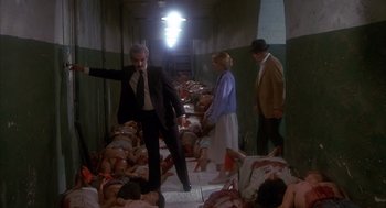 Movie still from “Missing” (1982), directed by Costa-Gavras – A group of people standing in a room covered in dead bodies; Wide shot, High angle