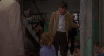 Movie still from “Missing” (1982), directed by Costa-Gavras – An older man in a hat is talking to a young woman; Medium shot, High angle