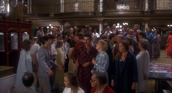 Movie still from “Missing” (1982), directed by Costa-Gavras – A group of people standing in a large room; Wide shot, High angle
