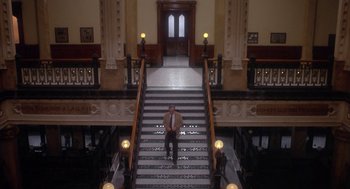 Movie still from “Missing” (1982), directed by Costa-Gavras – A man in a suit and tie sitting on the steps of a building; Extreme Wide shot, High angle