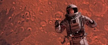Movie still from “Mission to Mars” (2000), directed by Brian De Palma – A man in a spacesuit standing in front of a red planet; Medium shot, Overhead angle