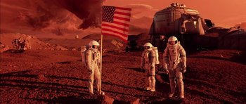 Movie still from “Mission to Mars” (2000), directed by Brian De Palma – A group of people on a dirt field with an american flag on it; Wide shot, Low angle