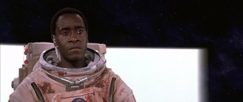 Movie still from “Mission to Mars” (2000), directed by Brian De Palma – A man in a spacesuit is standing in front of a space background; Close Up shot, Low angle