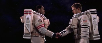 Movie still from “Mission to Mars” (2000), directed by Brian De Palma – Two men in spacesuits shaking hands in front of a star filled sky; Medium shot, Low angle