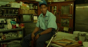 Movie still from “Mississippi Masala” (1991), directed by Mira Nair – A man sitting on a chair in a room; Medium shot, Low angle