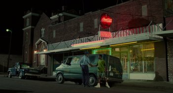 Movie still from “Mississippi Masala” (1991), directed by Mira Nair – Two men standing in front of a van in front of a building; Extreme Wide shot, Low angle