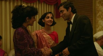 Movie still from “Mississippi Masala” (1991), directed by Mira Nair – Two women and a man shaking hands in a room; Medium shot, Over the shoulder angle