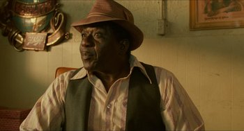 Movie still from “Mississippi Masala” (1991), directed by Mira Nair – An older man wearing a brown hat and a striped shirt; Close Up shot, Low angle