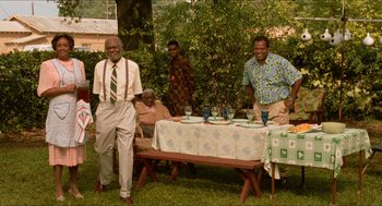Movie still from “Mississippi Masala” (1991), directed by Mira Nair – A group of people sitting at a table in a yard; Wide shot, High angle