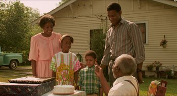 Movie still from “Mississippi Masala” (1991), directed by Mira Nair – An older man cutting a birthday cake for a young boy; Medium shot, Over the shoulder angle