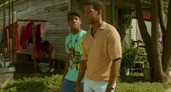 Movie still from “Mississippi Masala” (1991), directed by Mira Nair – Two young men standing next to each other in front of a house; Medium shot, Over the shoulder angle