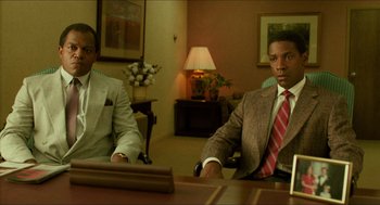 Movie still from “Mississippi Masala” (1991), directed by Mira Nair – Two men in suits sitting at a table in front of a lamp; Medium shot, Low angle