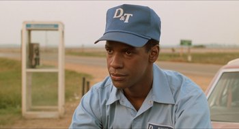 Movie still from “Mississippi Masala” (1991), directed by Mira Nair – A man wearing a hat sitting on the side of a road; Close Up shot, Low angle