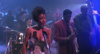 Movie still from “Mo' Better Blues” (1990), directed by Spike Lee – A woman holding a microphone while standing next to a man playing a saxophone; Medium shot, Over the shoulder angle