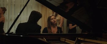 Movie still from “Molly's Game” (2017), directed by Aaron Sorkin – A woman sitting in front of a grand piano in a room; Medium shot, Over the shoulder angle