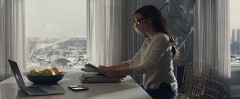 Movie still from “Molly's Game” (2017), directed by Aaron Sorkin – A woman sitting at a table with a stack of newspapers; Medium shot, Over the shoulder angle