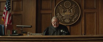 Movie still from “Molly's Game” (2017), directed by Aaron Sorkin – A man in a judge's robe is sitting at a podium; Medium shot, Low angle
