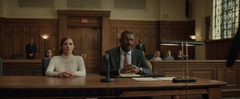 Movie still from “Molly's Game” (2017), directed by Aaron Sorkin – A man sitting at a table in front of a microphone; Medium shot, Low angle