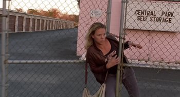 Movie still from “Monster” (2003), directed by Patty Jenkins – A woman holding onto a chain link fence while holding a purse; Medium shot, Low angle