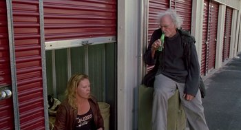 Movie still from “Monster” (2003), directed by Patty Jenkins – A man and a woman sitting next to each other in front of a garage door; Medium shot, Low angle