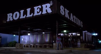 Movie still from “Monster” (2003), directed by Patty Jenkins – A man sitting on a skateboard in front of a roller skate shop; Wide shot, Low angle
