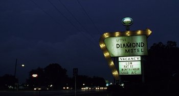 Movie still from “Monster” (2003), directed by Patty Jenkins – A lit up diamond motel sign at night time; Extreme Wide shot, Low angle