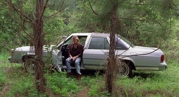 Movie still from “Monster” (2003), directed by Patty Jenkins – A man sitting on the ground next to a silver car; Wide shot, Low angle