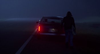 Movie still from “Monster” (2003), directed by Patty Jenkins – A person walking on the side of a road near a car; Wide shot, Over the shoulder angle