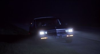 Movie still from “Monster” (2003), directed by Patty Jenkins – A car driving down a street at night with headlights on; Wide shot, Low angle