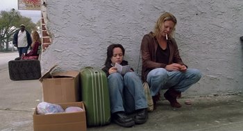 Movie still from “Monster” (2003), directed by Patty Jenkins – Two women sitting on the ground with their luggage; Wide shot, Low angle