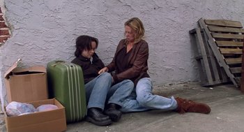 Movie still from “Monster” (2003), directed by Patty Jenkins – A woman sitting on the ground next to a woman holding a suitcase; Medium shot, High angle