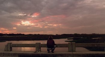 Movie still from “Monster” (2003), directed by Patty Jenkins – A woman sitting on a bridge looking at the sky; Extreme Wide shot, Over the shoulder angle