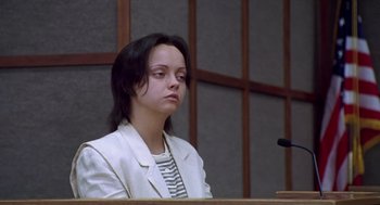 Movie still from “Monster” (2003), directed by Patty Jenkins – A woman in a white jacket sitting in front of a microphone; Medium shot, Low angle
