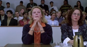 Movie still from “Monster” (2003), directed by Patty Jenkins – A woman sitting in front of an audience with her hands clasped behind her neck; Medium shot, Low angle