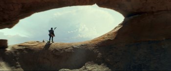Movie still from “Monster Hunter” (2020), directed by Paul W.S. Anderson – A man standing on a rock formation holding a guitar; Extreme Wide shot, Low angle