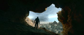 Movie still from “Monster Hunter” (2020), directed by Paul W.S. Anderson – A man standing on top of a mountain looking out a cave; Extreme Wide shot, Low angle