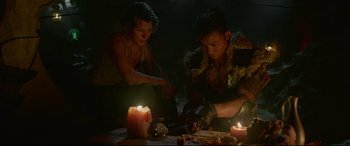 Movie still from “Monster Hunter” (2020), directed by Paul W.S. Anderson – A couple of people sitting next to some candles; Medium shot, High angle