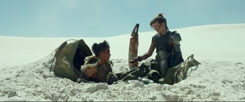 Movie still from “Monster Hunter” (2020), directed by Paul W.S. Anderson – Two people sitting on the ground in the sand; Wide shot, Over the shoulder angle