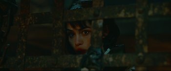 Movie still from “Monster Hunter” (2020), directed by Paul W.S. Anderson – A woman is looking through a metal fence; Close Up shot, High angle