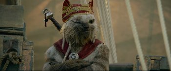 Movie still from “Monster Hunter” (2020), directed by Paul W.S. Anderson – A cat wearing a crown and holding a sword; Close Up shot, Over the shoulder angle