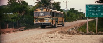 Movie still from “Monsters” (2010), directed by Gareth Edwards – A yellow and green school bus driving down a dirt road; Extreme Wide shot, High angle