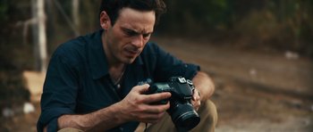 Movie still from “Monsters” (2010), directed by Gareth Edwards – A man sitting down holding a camera in his hands; Close Up shot, High angle