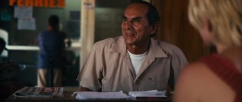 Movie still from “Monsters” (2010), directed by Gareth Edwards – An older man sitting at a table with papers in front of him; Medium shot, Over the shoulder angle