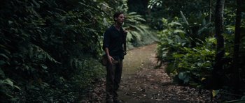 Movie still from “Monsters” (2010), directed by Gareth Edwards – A man standing on a dirt path in the woods; Medium shot, Over the shoulder angle