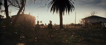 Movie still from “Monsters” (2010), directed by Gareth Edwards – Two people standing in the dirt near a palm tree; Extreme Wide shot, Low angle