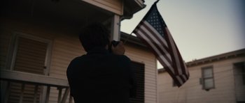 Movie still from “Monsters” (2010), directed by Gareth Edwards – A person holding a camera in front of an american flag; Medium shot, Low angle